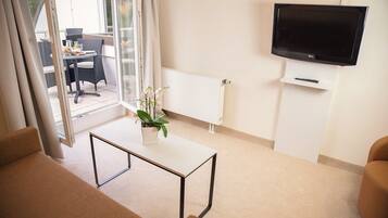 Una sala de estar moderna con un televisor de pantalla plana, un radiador blanco y una orquídea en maceta sobre una mesa blanca.