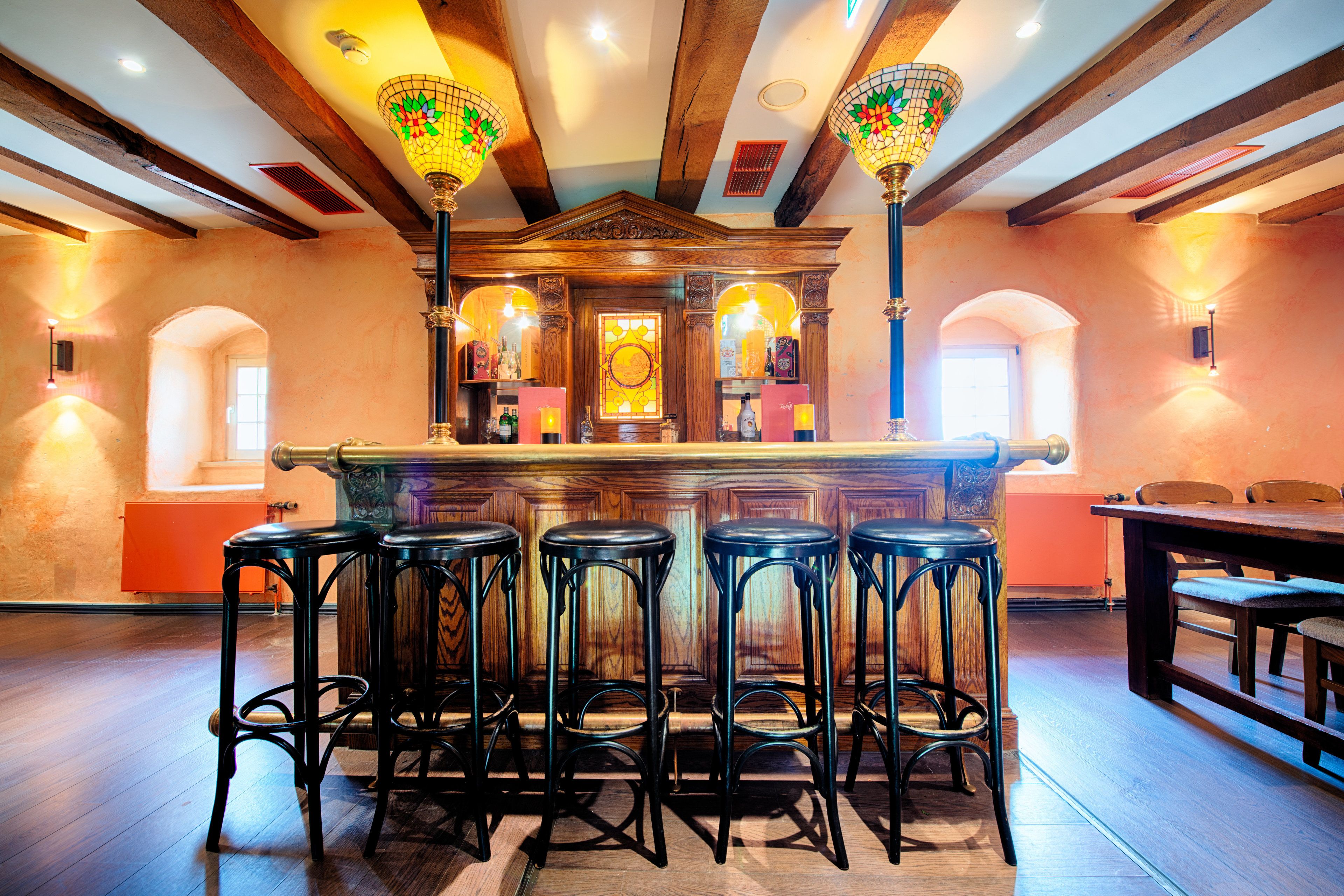 Eine Bar mit Holzbalken, einer Theke in der Mitte und vier Hockstühlen.