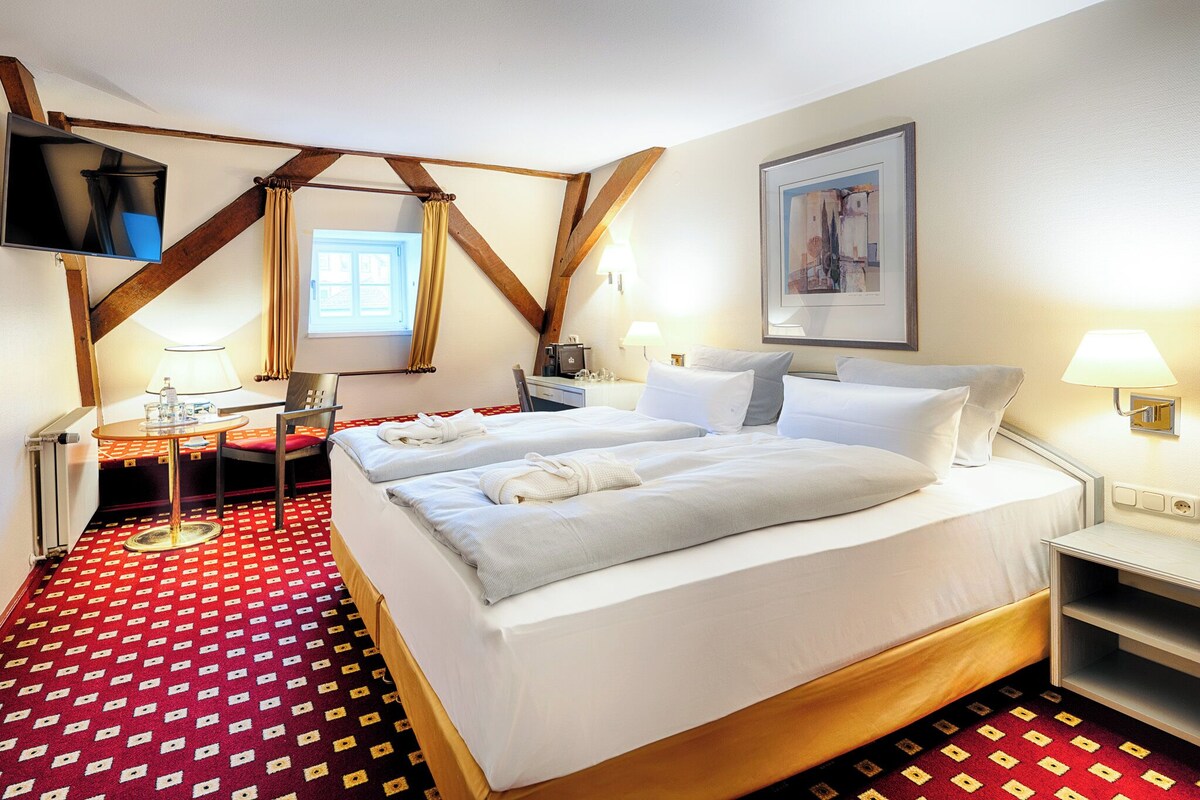 Une chambre d’hôtel avec un grand lit, un bureau, une chaise, une télévision et une fenêtre avec des rideaux.