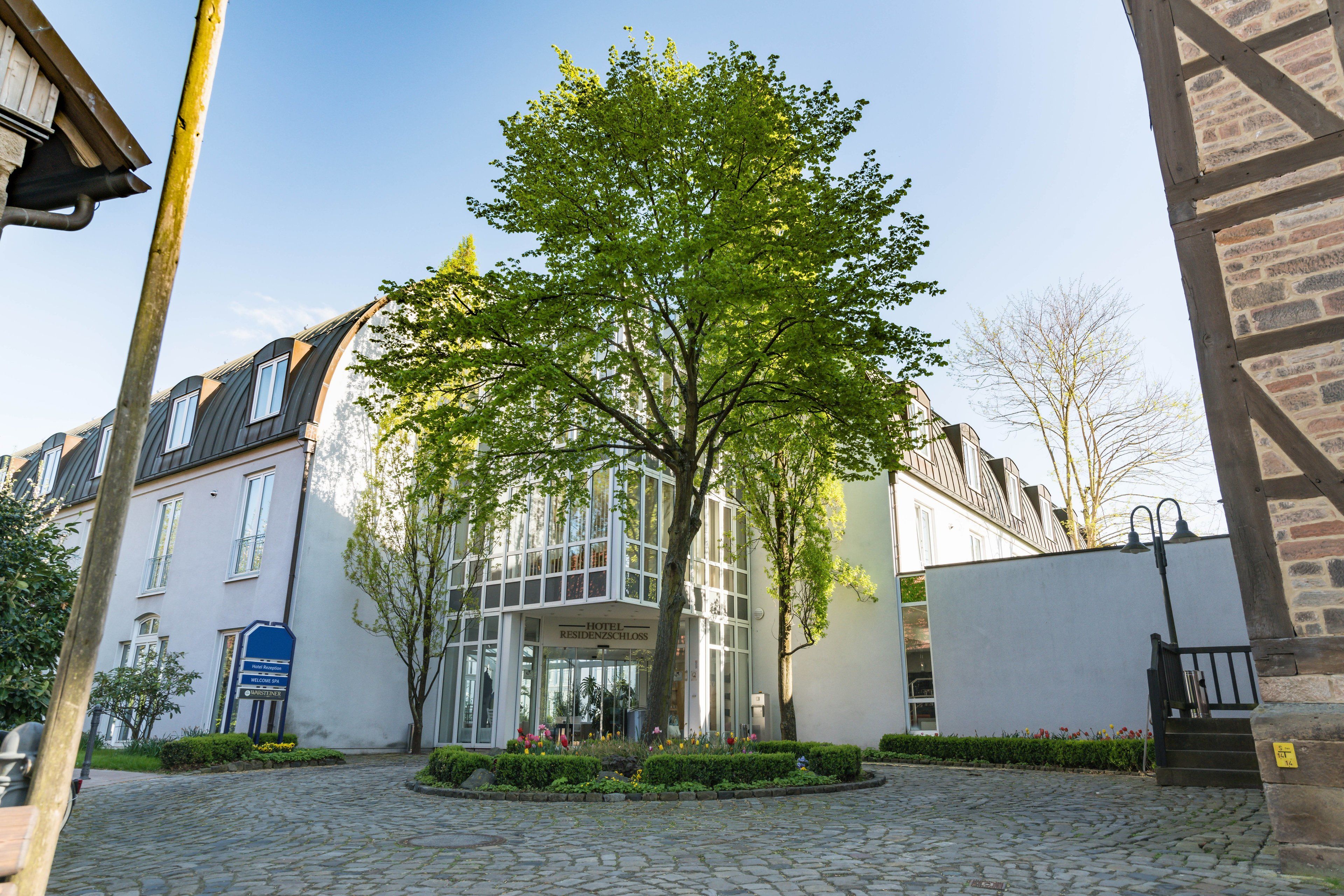 Een hotel met een centrale glazen gevel, omringd door kinderaardewerktegels en een boom.