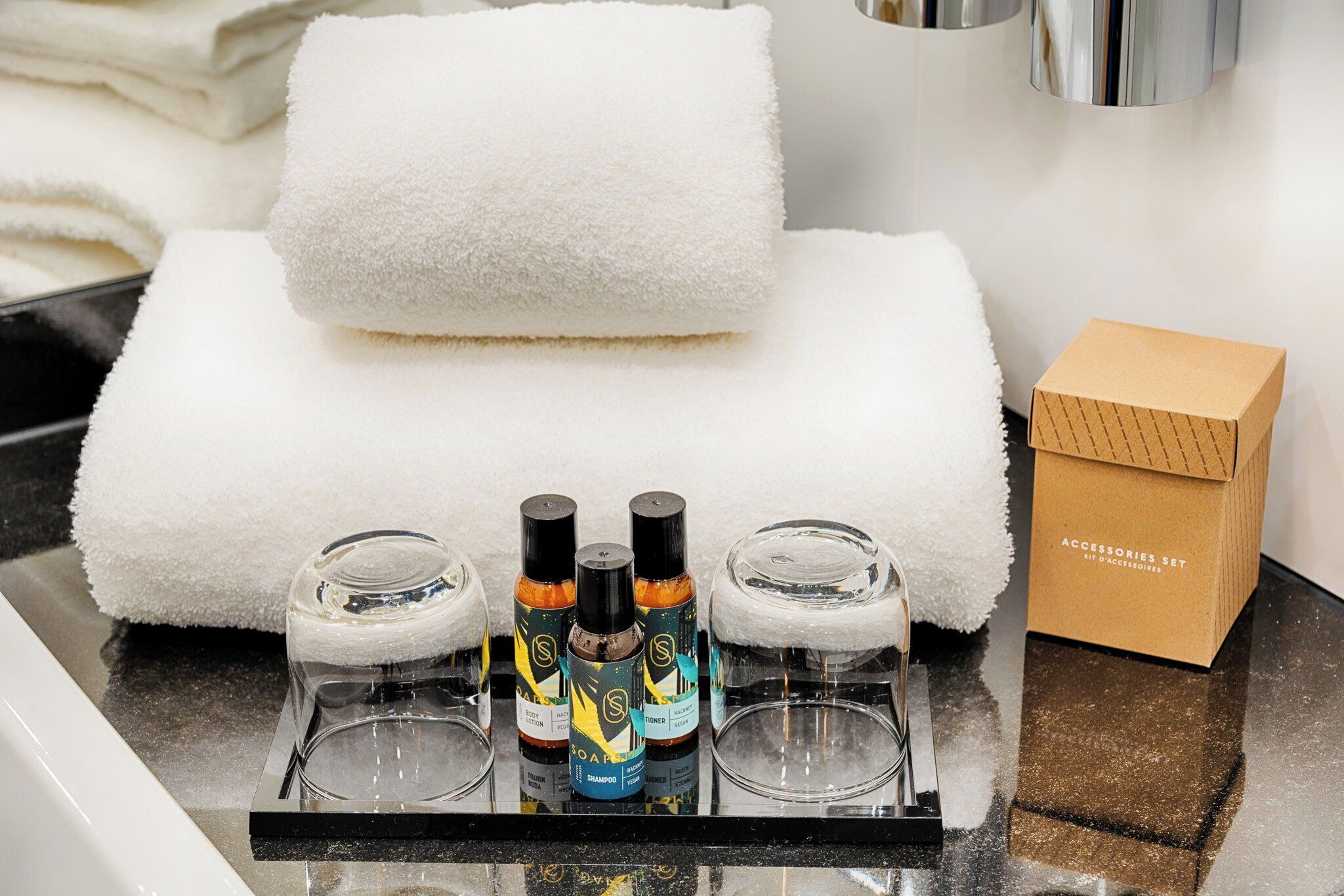 A bathroom counter with toiletries, a white towel, and a box labeled "ACCESSORIES SET."