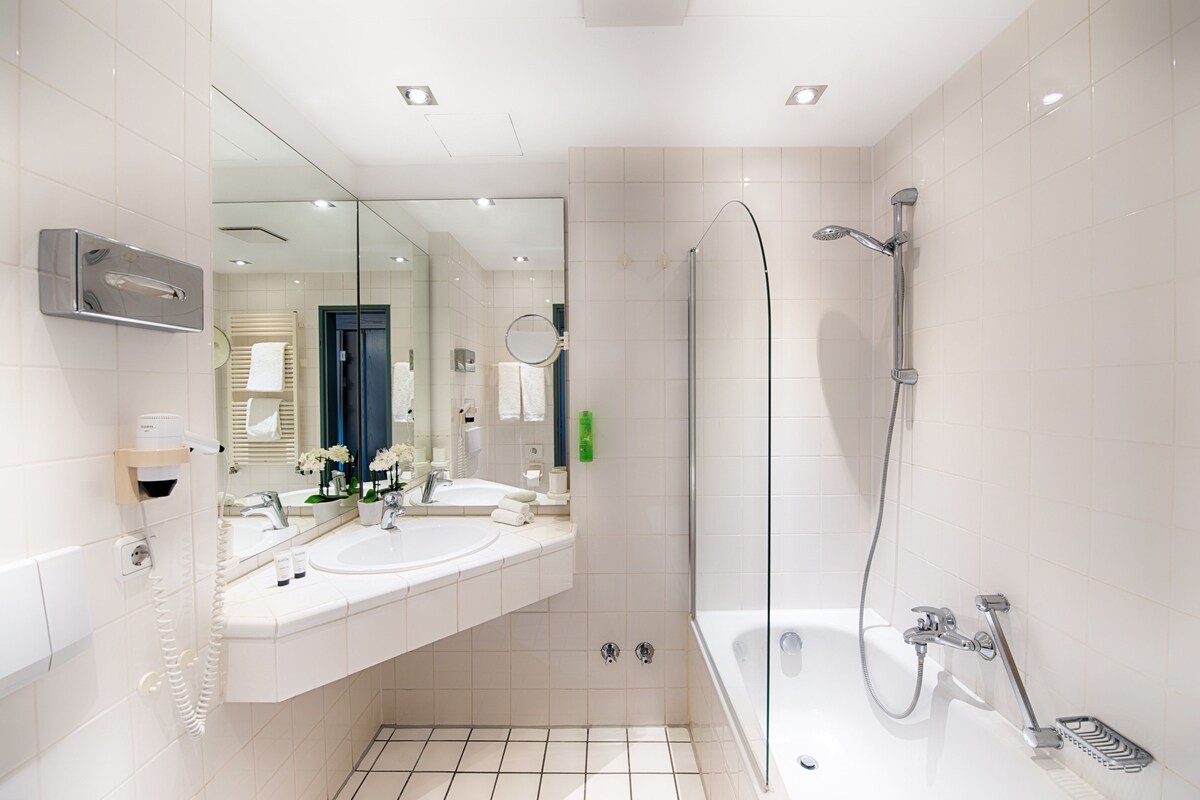 Une salle de bain moderne dotée d’un double lavabo, d’un grand miroir, d’une douche avec un pommeau de douche amovible et de toilettes intégrées.