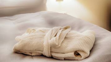 A neatly folded white bathrobe on a bed with a light-colored pillow and a wall-mounted light fixture.