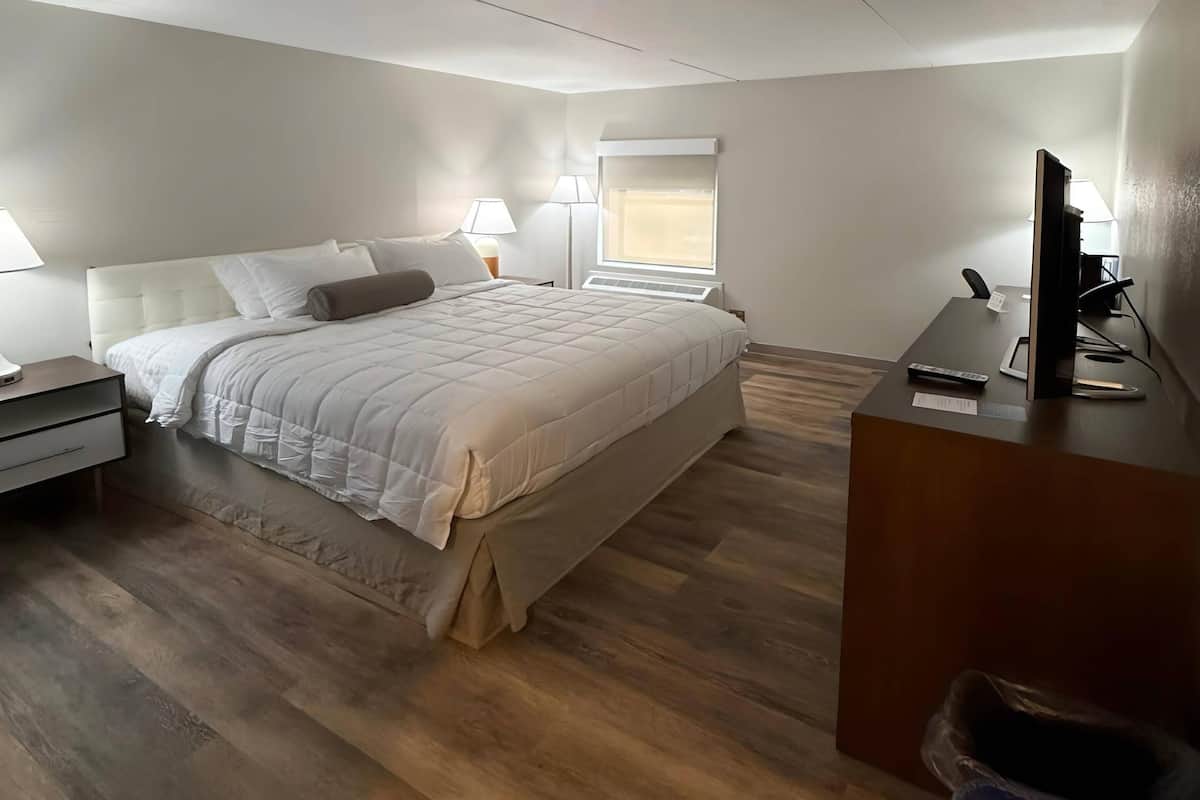 A hotel room with a bed, bedside lamps, a desk with a computer, and a window.