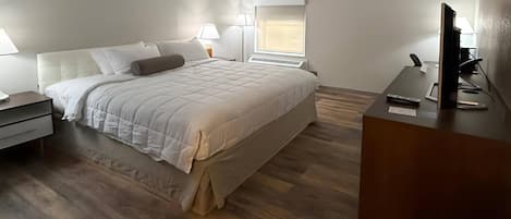 A hotel room with a bed, bedside lamps, a desk with a computer, and a window.