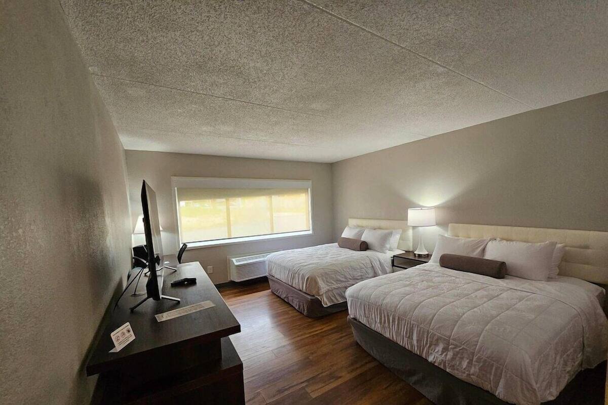 A hotel room with two beds, a desk with a computer, a window, and a ceiling with a textured pattern.