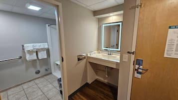 A hotel bathroom with a shower, a sink, a mirror, and a door with a fire evacuation map.