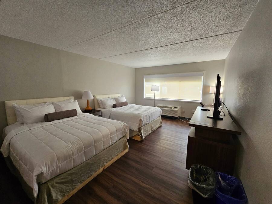 Ett hotellrum med två sängar, ett skrivbord med en dator, ett fönster med persienner och en ventil i taket.
