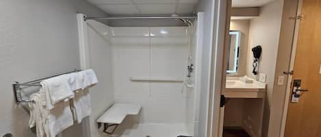 Een badkamer met een douche, handdoekhouder, wastafel en een prullenbak.