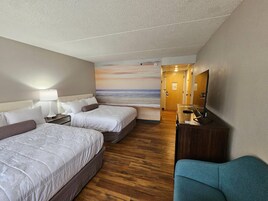 Habitación de hotel con dos camas, un escritorio, una silla y un mural de una playa.