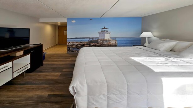 Habitación de hotel con cama, televisión, escritorio y vista a un faro a través de un mural.