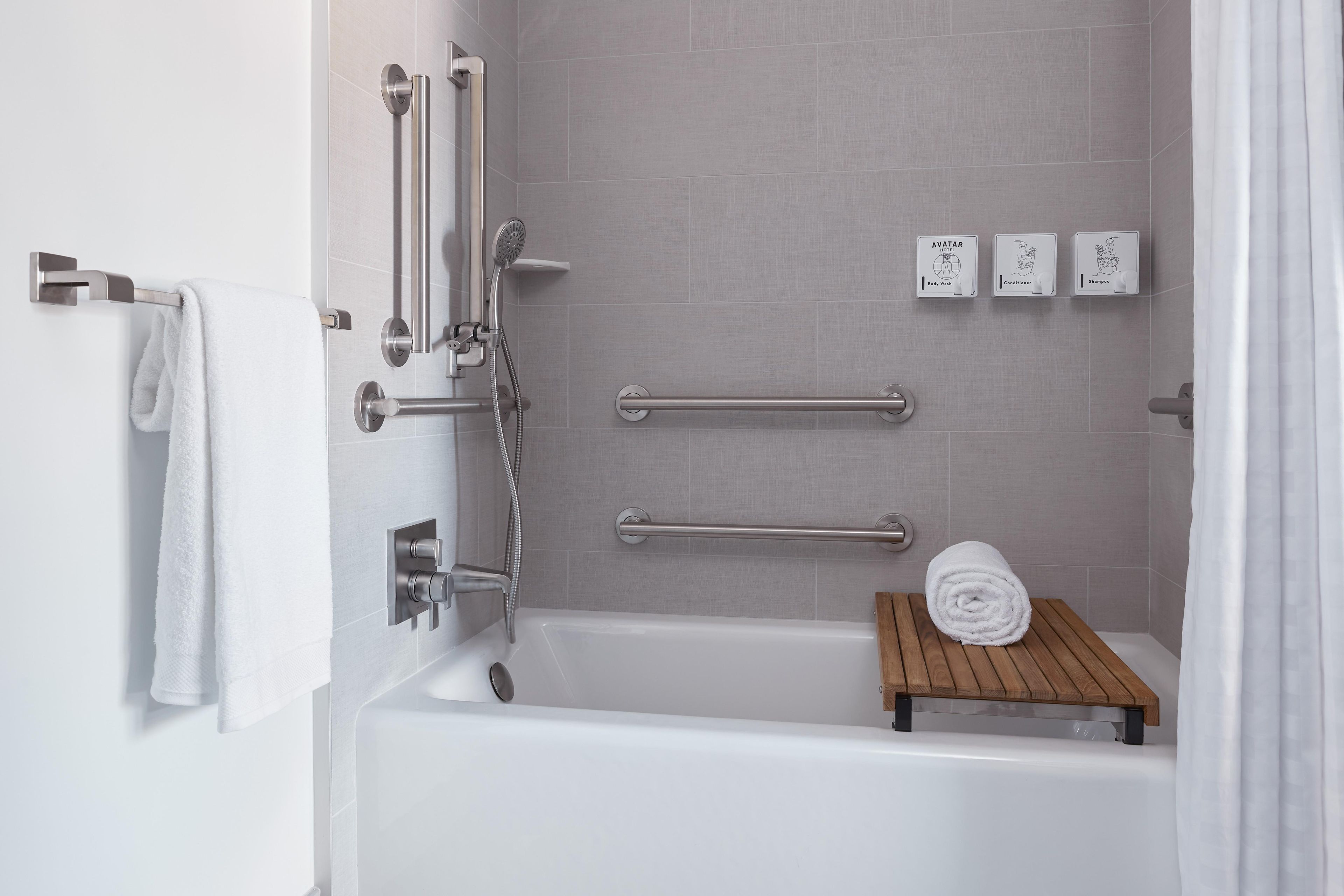A modern bathroom with a bathtub, grab bars, a towel rack, and a wooden shelf.