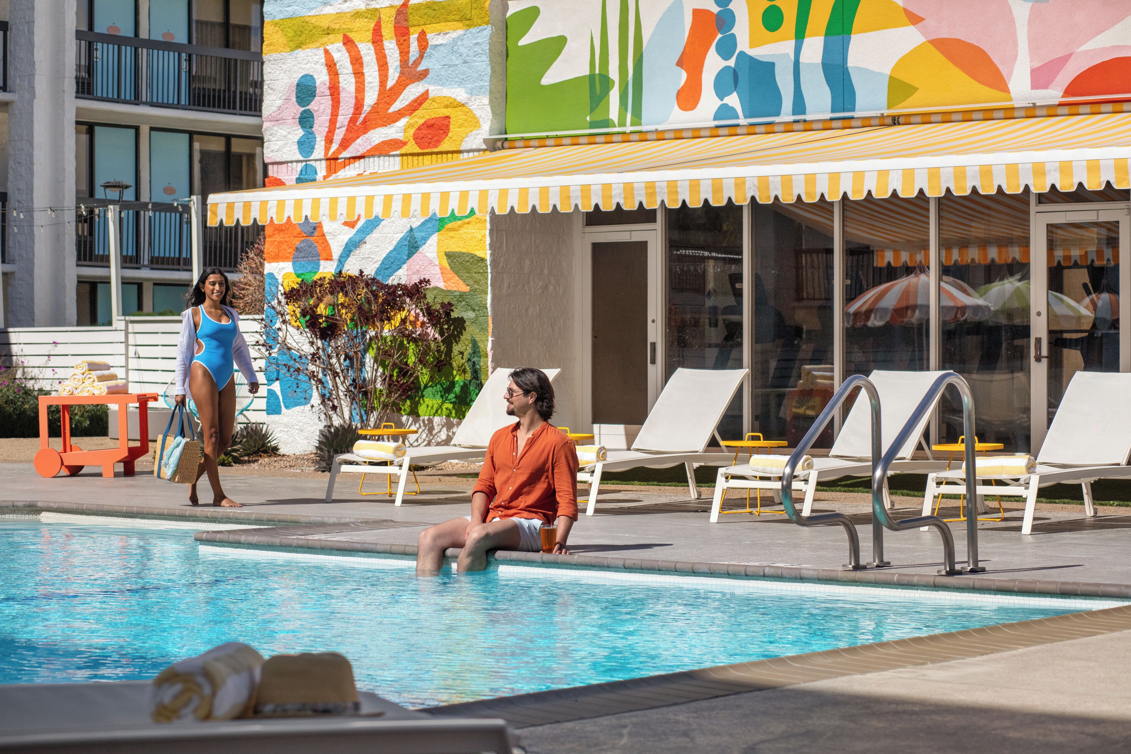 A pool area with lounge chairs and a colorful mural on the building.