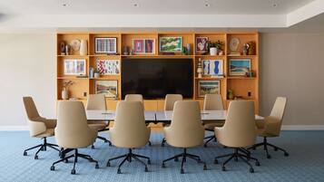 A conference room with a large flat-screen TV, beige chairs, and a wooden shelf with various decorative items.