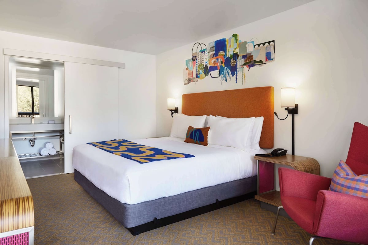 A hotel room with a bed, a chair, a desk, and a mirror.