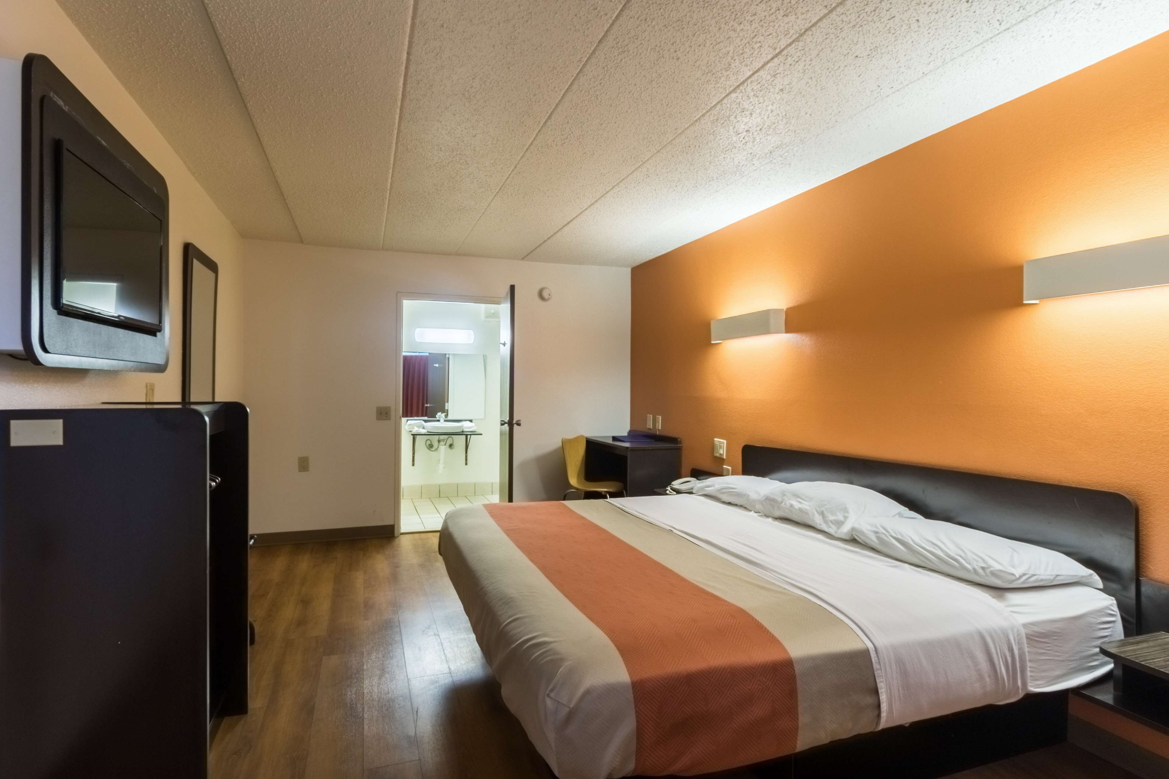 A hotel room with a bed, a desk, a chair, a TV, and a refrigerator.