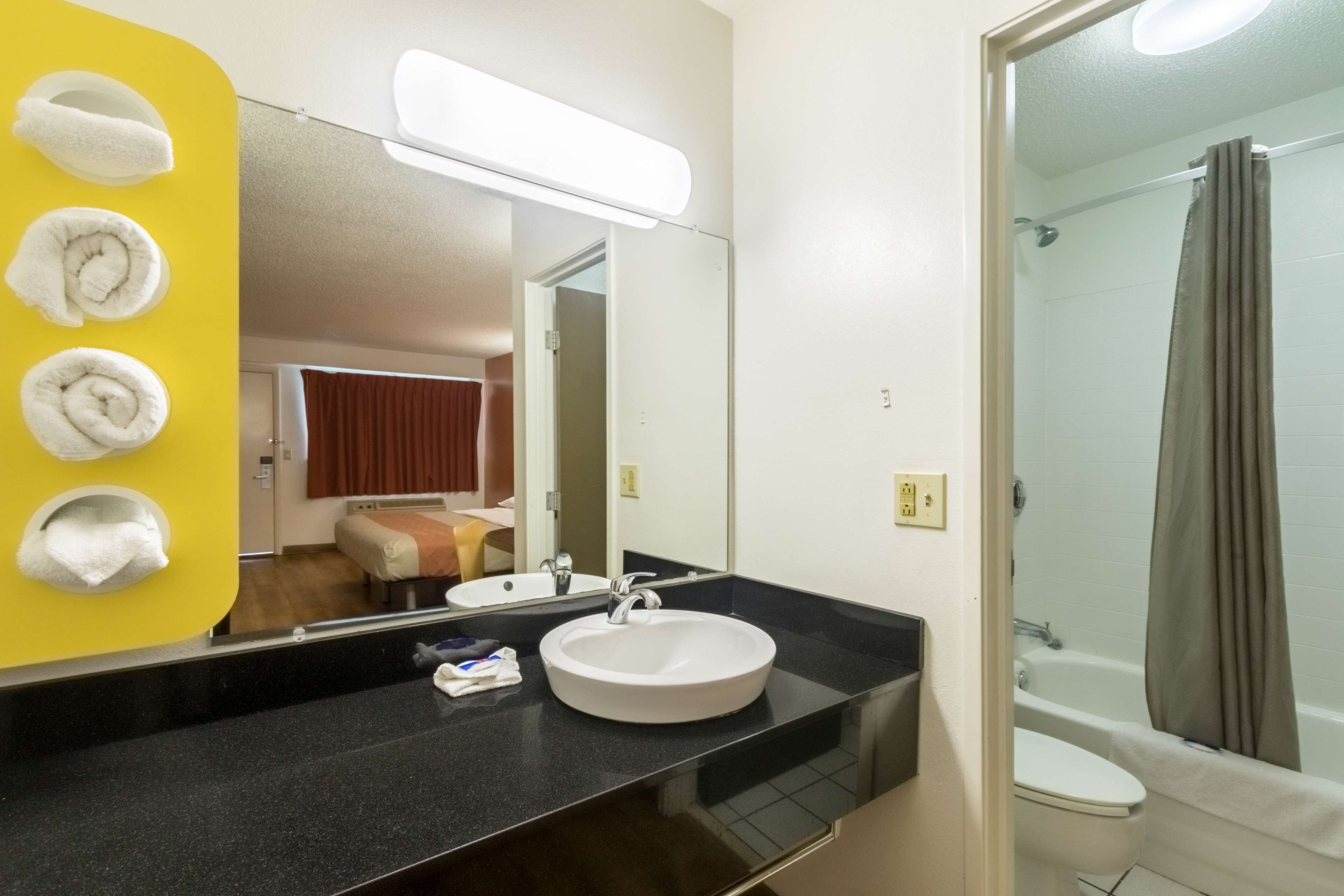 A bathroom with a sink, mirror, and a shower. There are towels hanging on a yellow wall.