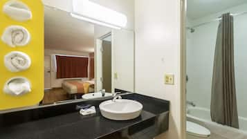 A bathroom with a sink, mirror, and a shower. There are towels hanging on a yellow wall.