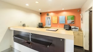 A reception desk with a computer, a printer, and a wall clock. There are three signs on the wall. - Motel 6 Crawfordsville, IN (Crawfordsville)
