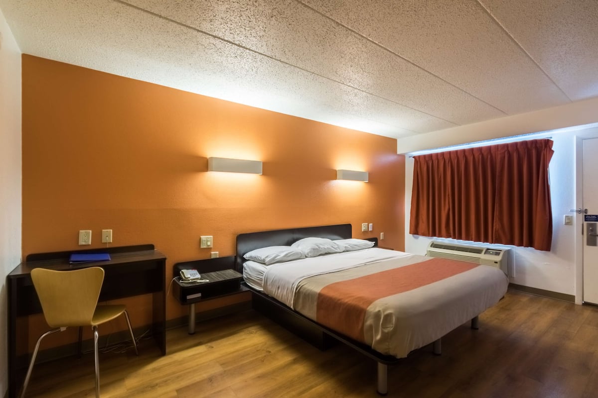 A hotel room with a bed, desk, chair, and a window with curtains.