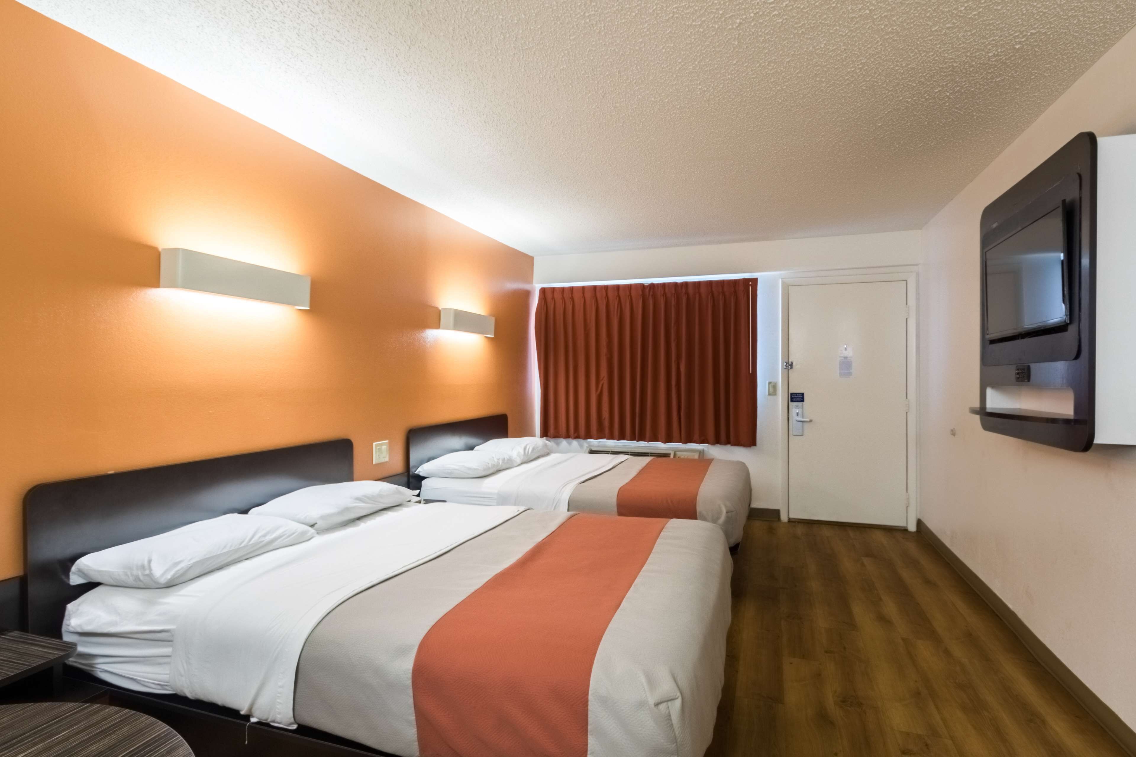 A hotel room with two beds, a flat-screen TV, and a door leading to a bathroom.