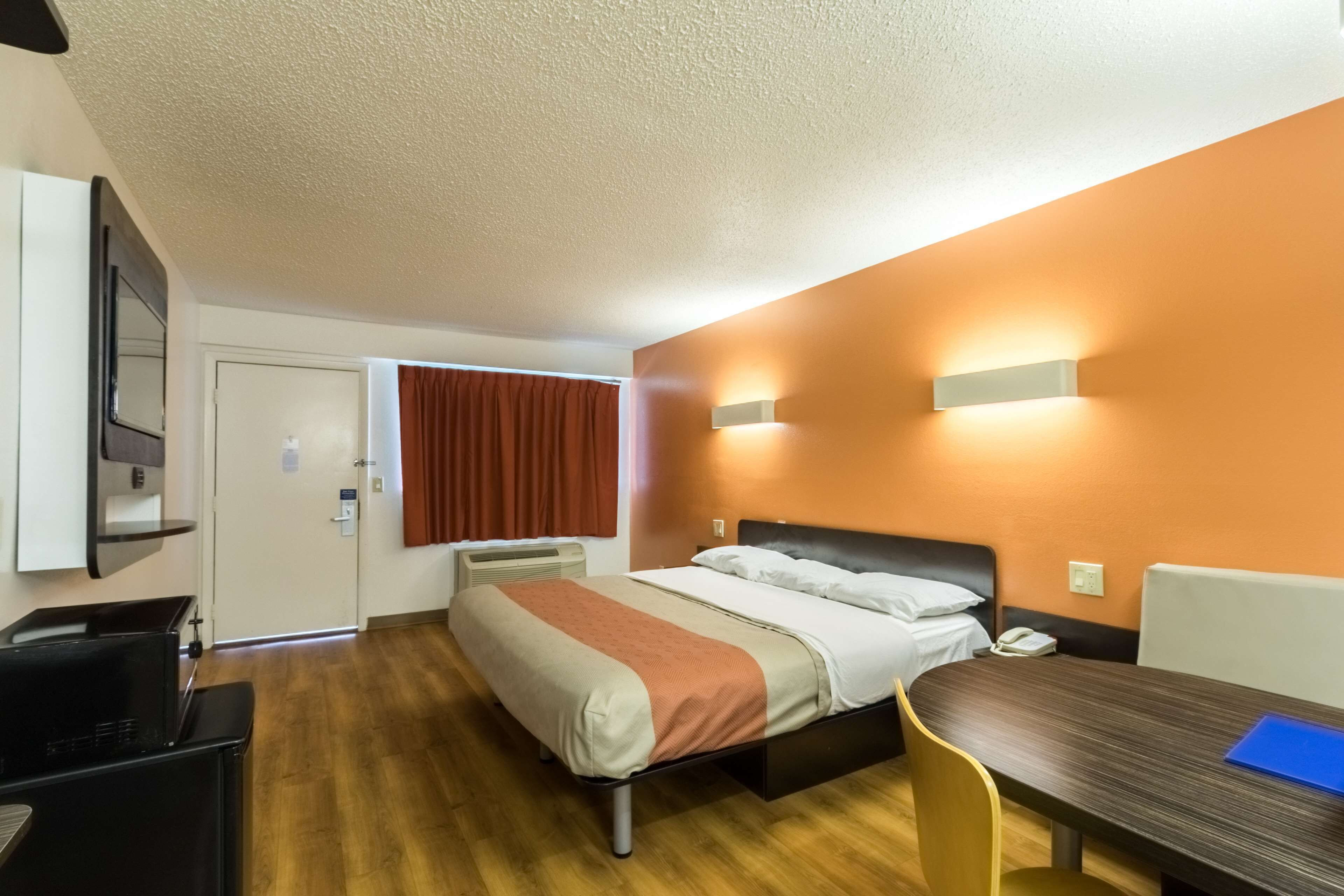 A hotel room with a bed, a desk, a chair, a TV, and a window with curtains.