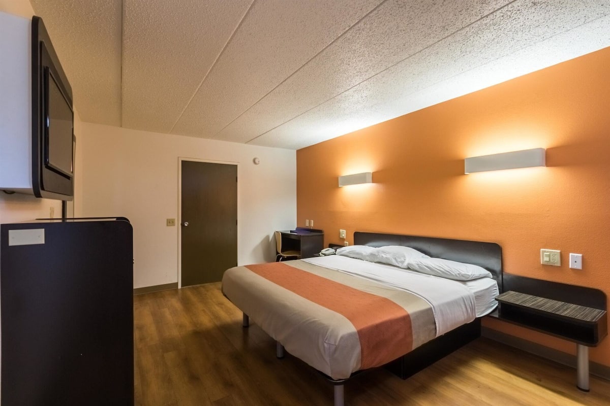 A hotel room with a bed, a desk, a chair, a TV, and a door.