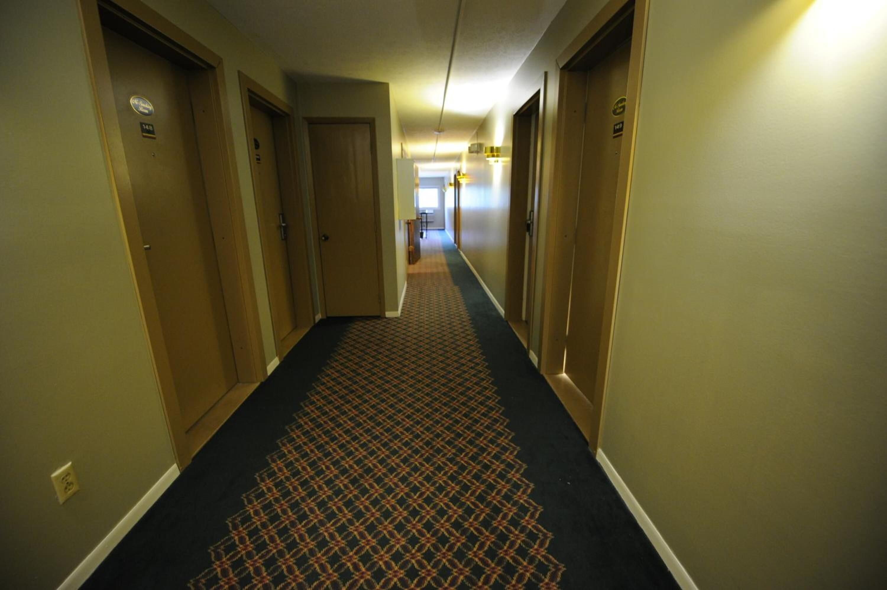 A hotel hallway with carpeted floors, doors on both sides, and a light fixture on the ceiling.