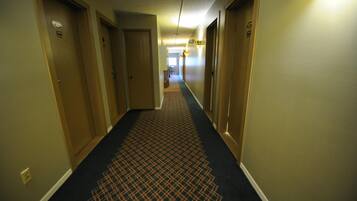 A hotel hallway with carpeted floors, doors on both sides, and a light fixture on the ceiling.