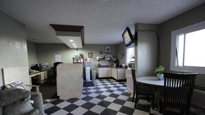 Una cocina compacta con piso a cuadros, una mesa de comedor con sillas, un sofá y un televisor montado en la pared.