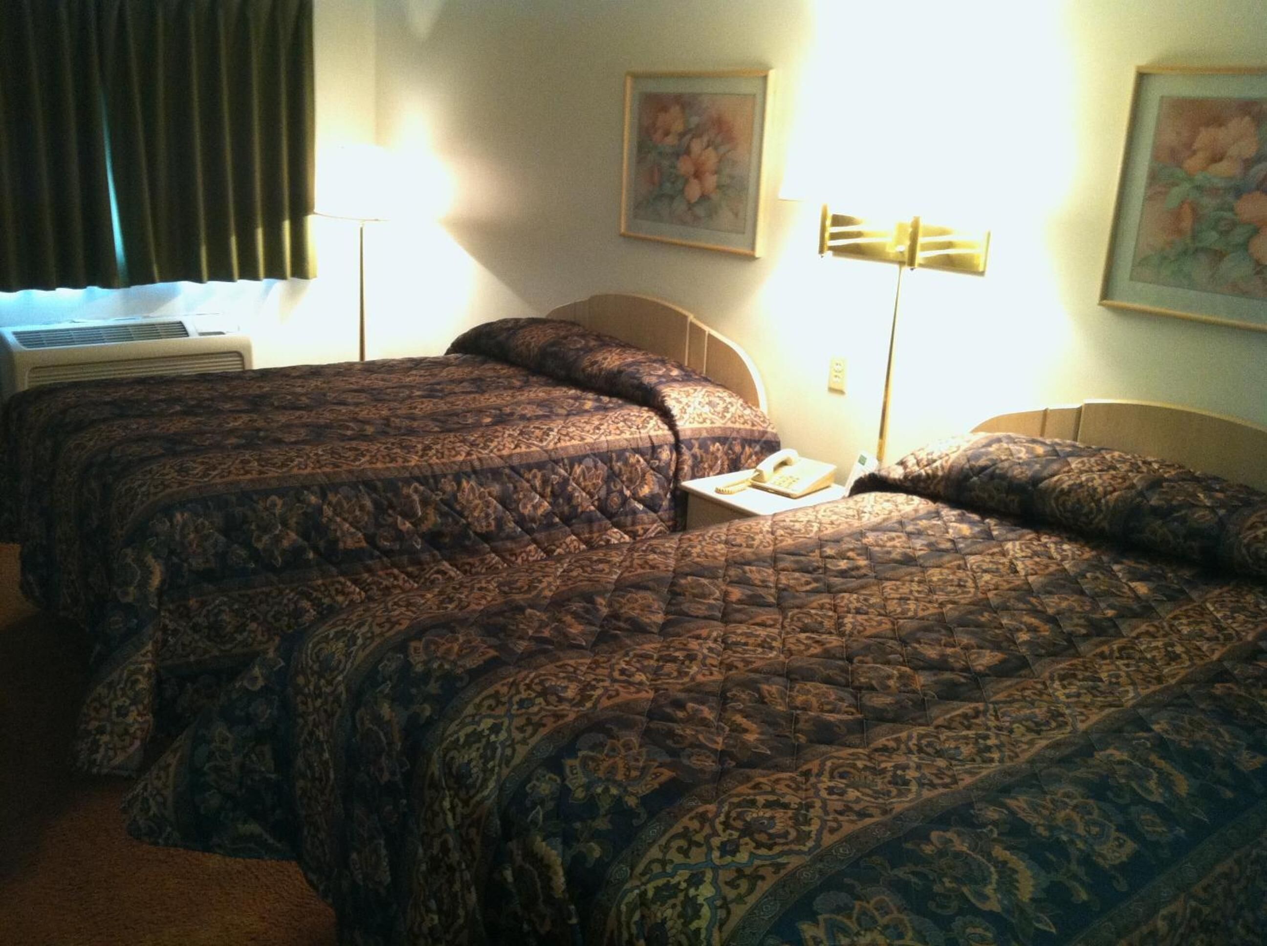 Habitación de hotel con tres camas dobles, teléfono junto a la cama y aire acondicionado instalado en la pared.