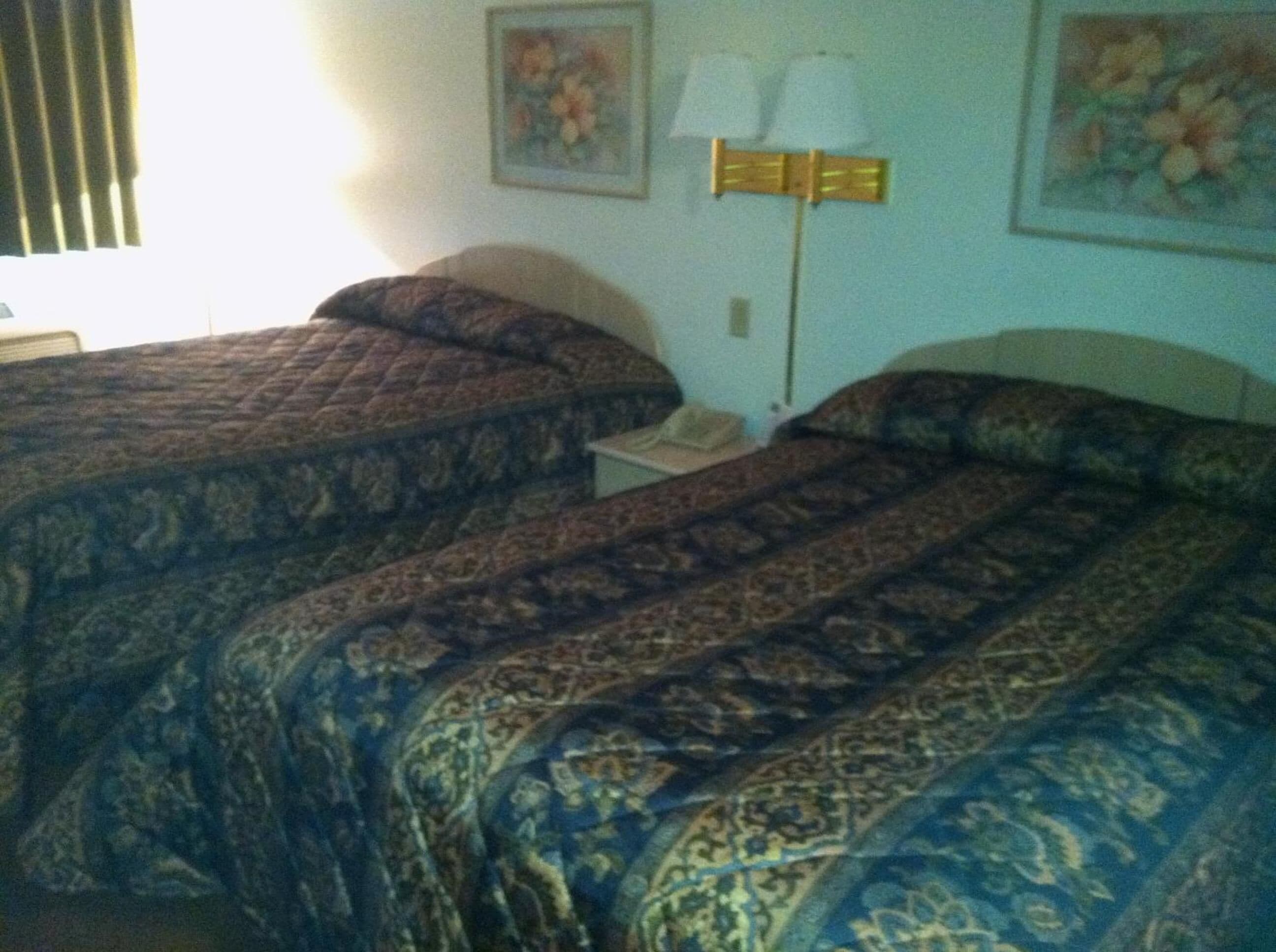 A hotel room with two beds, a nightstand, a lamp, and floral wall art.