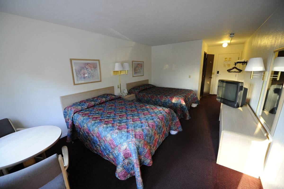 A hotel room with two beds, a desk, a chair, a TV, and a mirror.