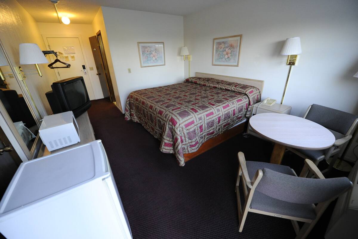 A hotel room with a bed, a desk, a chair, a television, and a lamp.