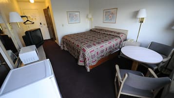 Et hotelværelse med en seng, et skrivebord, en stol, et fjernsyn og en lampe.