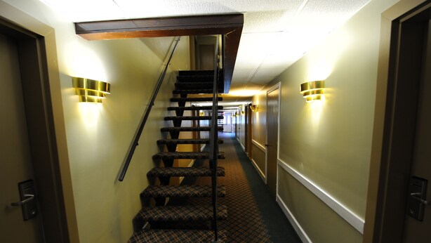 Un pasillo de hotel con una escalera alfombrada, apliques en la pared y puertas a ambos lados.