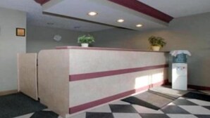 Un mostrador de recepción con un piso estampado en cuadros, un reloj en la pared y una planta en maceta encima.