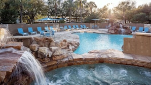 A pool area with a waterfall, lounge chairs, and a stone wall. - Sonesta Hotel Houston IAH Airport (Houston)