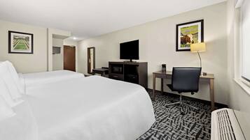 Una habitación de hotel con dos camas, un escritorio con silla, televisor y lámpara.