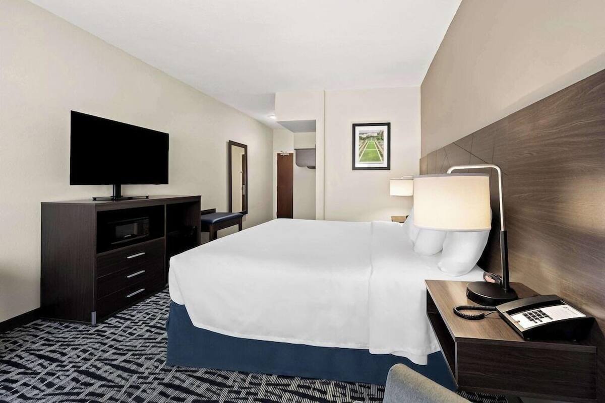 A hotel room with a bed, a TV, a desk with a lamp, a telephone, and a mirror.