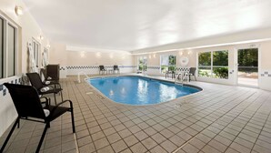 Una piscina interior con suelo de baldosas, sillas junto a la piscina y vistas al exterior a través de amplias ventanas.