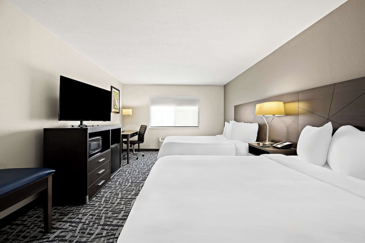 A hotel room with two beds, a desk with a TV, a chair, a lamp, and a window.