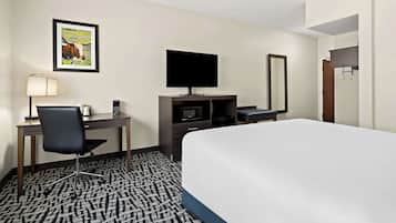 Habitación de hotel con cama, escritorio con silla, televisor de pantalla plana, microondas, espejo y un cuadro en la pared.