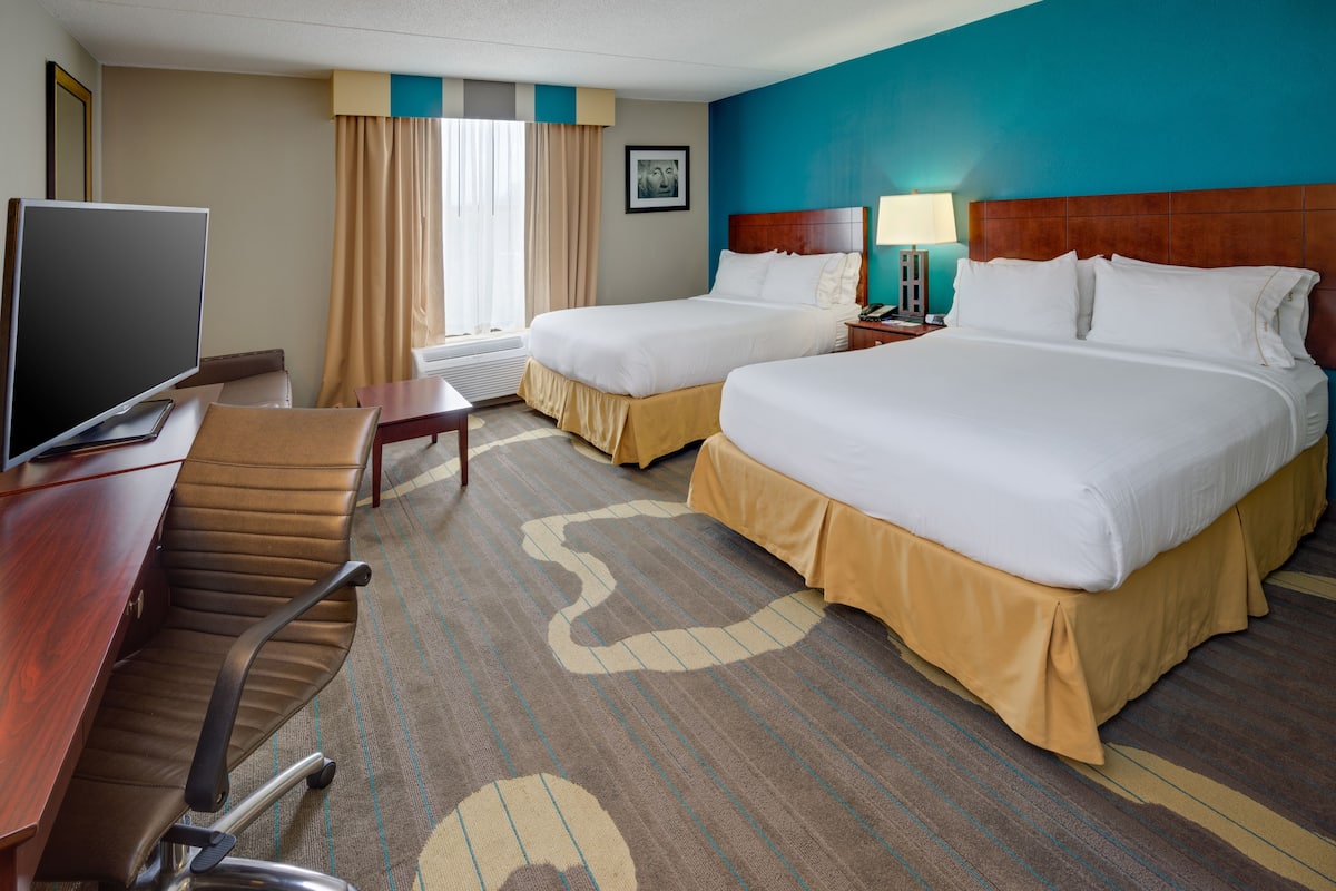 A hotel room with two beds, a desk with a computer, a chair, and a TV.