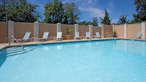 A swimming pool with multiple white lounge chairs and a clear blue sky in the background.