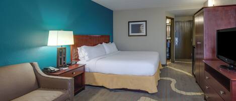 A hotel room with a bed, a desk with a lamp, a television, a sofa, and a carpet with a pattern.