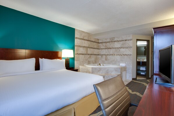 A hotel room with a large bed, a sitting area, a television, a bathroom with a sink and bathtub, and a view of the hallway. - Holiday Inn Express Washington DC East - Andrews AFB by IHG (Suitland)