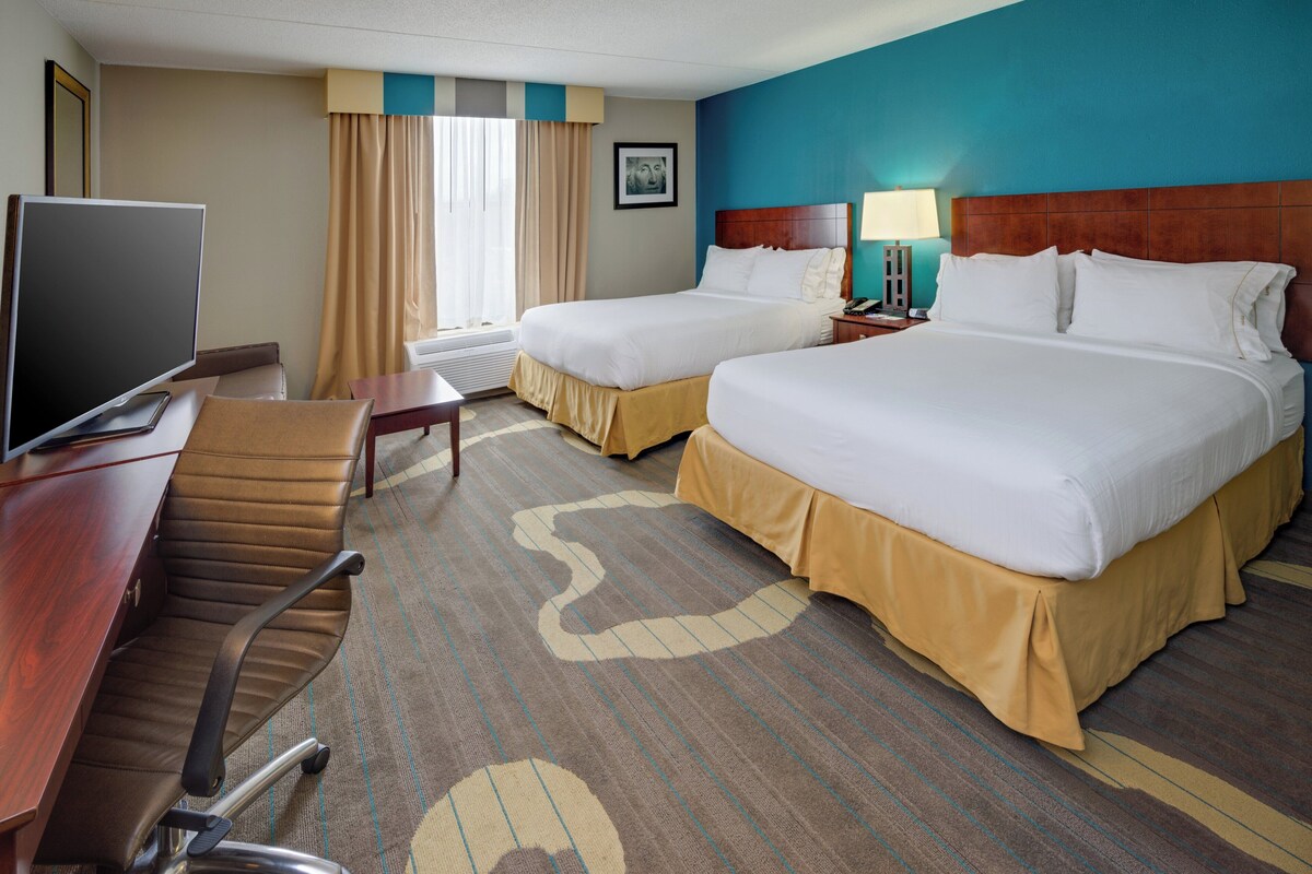 A hotel room with two beds, a desk with a computer, a chair, and a TV.