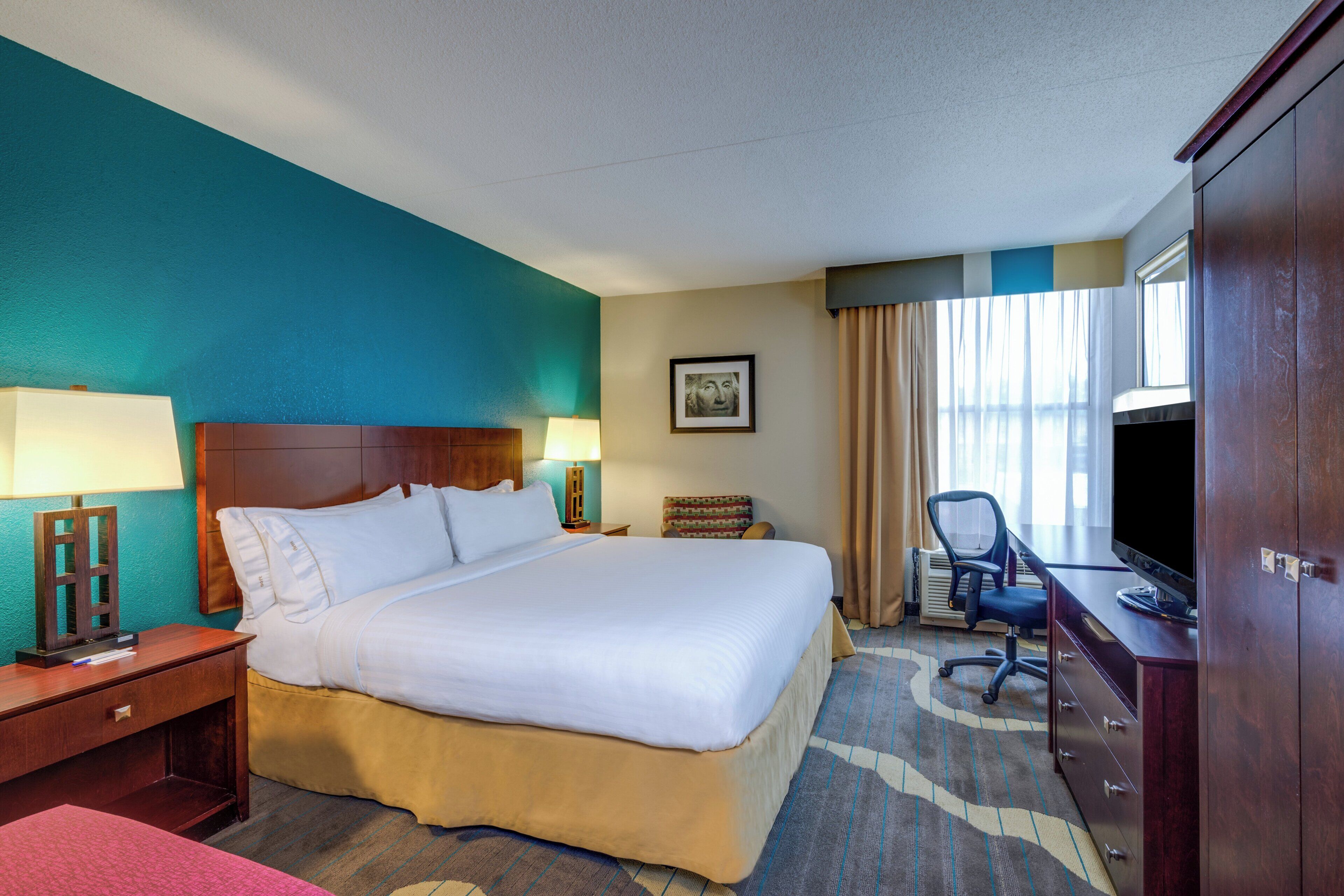A hotel room with a large bed, a desk, a chair, a television, and a picture on the wall.
