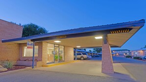 A motel with a covered parking area, a sign indicating a 'Caution & Clearance' zone, and a visible entrance with a window. - Suburban Studios near Mesa Verde (Cortez)